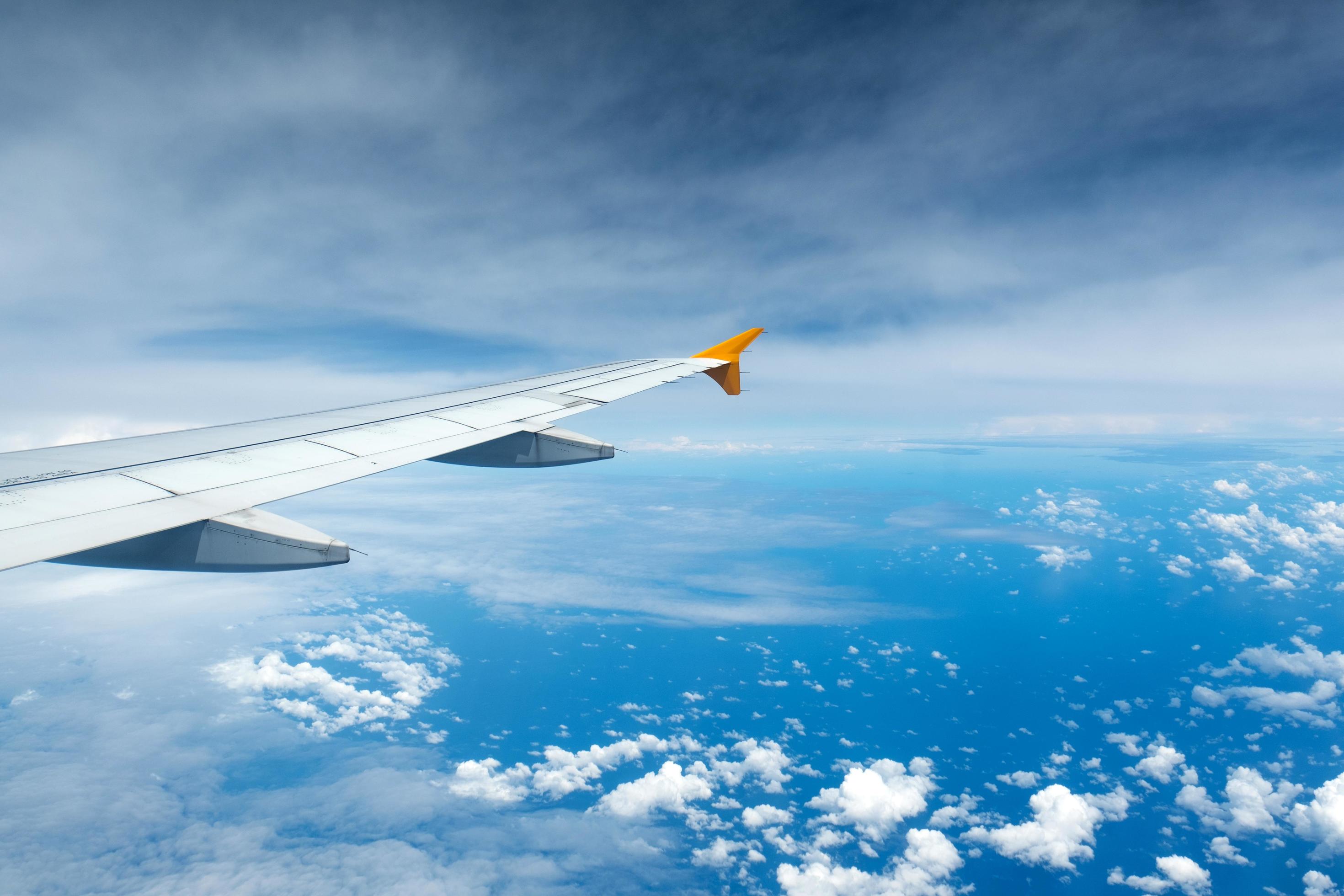 Airplane wing flying above clouds representing global travel